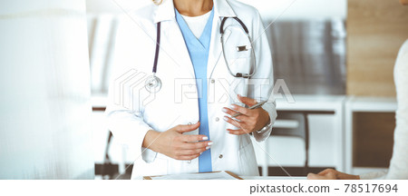 Unknown woman-doctor communicating with female patient in sunny clinic. Physician checks medical history record and exam results, close-up Unknown woman-doctor communicating with female patient in sunny clinic. Physician checks medical history record and exam results, close-up 78517694