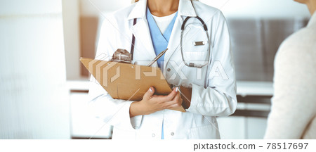 Unknown woman-doctor and patient in sunny hospital. Physician controls medication history records and exam results while using clipboard, close-up Unknown woman-doctor and patient in sunny hospital. Physician controls medication history records and exam results while using clipboard, close-up 78517697