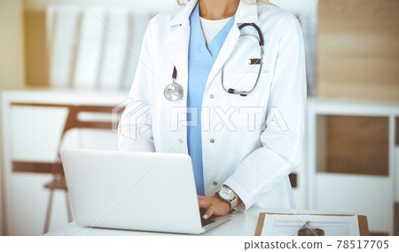 Unknown female physician using laptop computer, close-up. Woman-doctor at work in sunny clinic Unknown female physician using laptop computer, close-up. Woman-doctor at work in sunny clinic 78517705