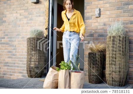 Housewife receiving groceries purchased online on the porch of her house Housewife receiving groceries purchased online on the porch of her house 78518131