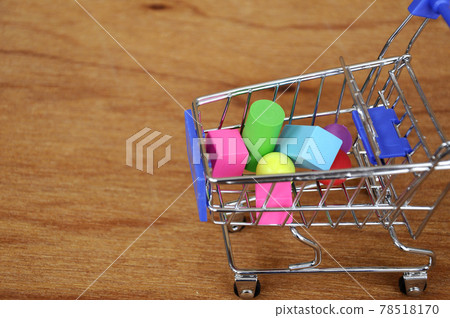 Colorful of rubber cube and other shapes inside toy shopping trolley with wood texture background.  78518170