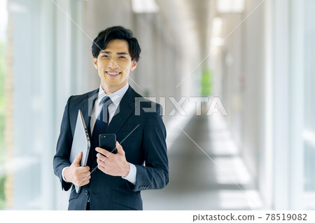 A businessman in a suit holding a smartphone in an office A businessman in a suit holding a smartphone in an office 78519082