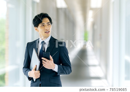 A businessman in a suit holding a smartphone in an office 78519085
