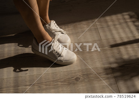 Close-up of female legs in white leather sneakers. 78519624