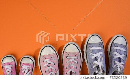 many multi-colored well-worn textile sneakers of different sizes on a orange background, top view 78520289
