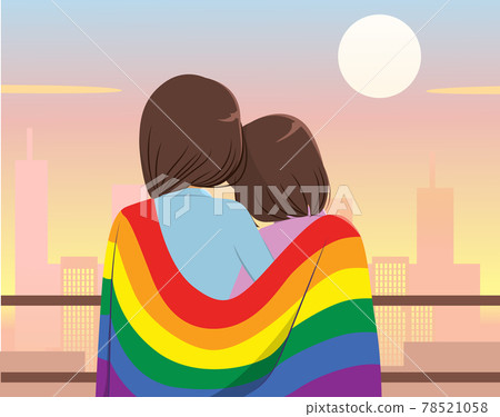 Lesbian couple wearing big LGBT flag on shoulders celebrating pride month looking back to city background 78521058