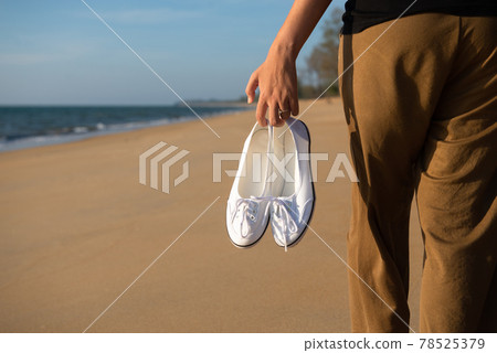 Woman hands holding shoes at the beach during sunset time,Back view 78525379