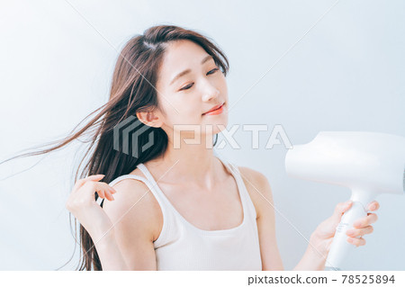 婦女用吹風機烘乾她的頭髮。 78525894