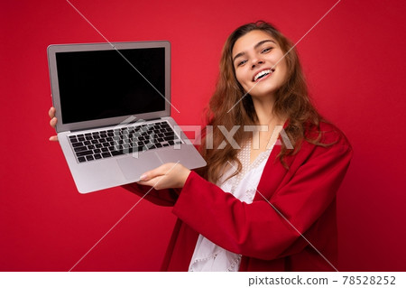 Photo of beautiful young woman holding computer laptop looking at camera isolated over colourful 78528252