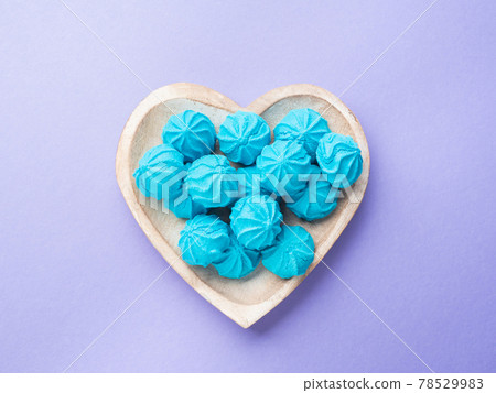 Heart shaped wooden dish with blue sweet meringues 78529983
