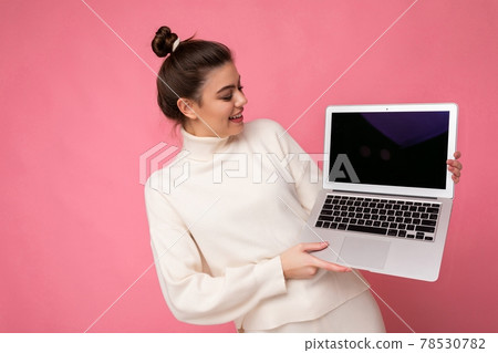Photo of beautiful girl with gathered brunette hair wearing white sweater holding computer laptop Photo of beautiful girl with gathered brunette hair wearing white sweater holding computer laptop 78530782