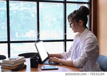 Side view of female student sitting in library and using laptop computer. Side view of female student sitting in library and using laptop computer. 78532184