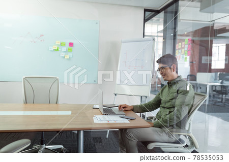 Smiling asian businessman sitting in meeting room using laptop seen through glass wall 78535053