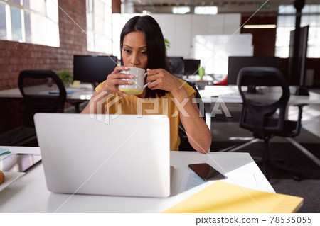 Caucasian businesswoman sitting at desk using laptop and drinking cup of coffee 78535055