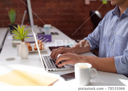 Midsection of caucasian businessman sitting at desk in office using laptop 78535066
