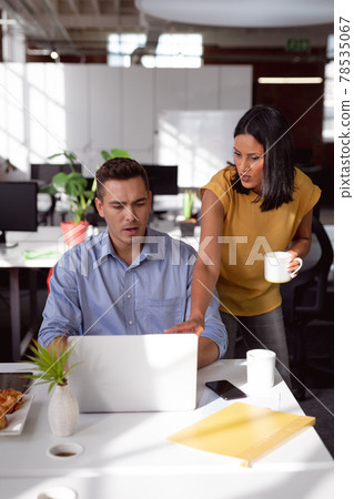 Caucasian male and female colleague in discussion at desk looking at laptop and drinking coffee 78535067