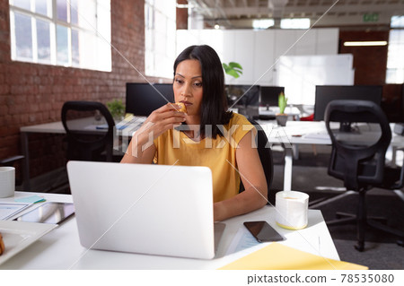 Caucasian businesswoman sitting at desk with coffee using laptop and biscuit 78535080