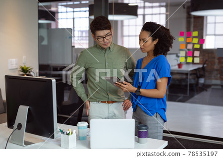 Diverse male and female colleague looking at tablet and discussing standing in office 78535197