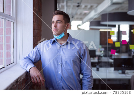 Portrait of thoughtful caucasian businessman in lowered face mask looking out of window 78535198