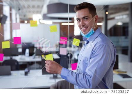 Portrait of caucasian businessman in lowered face mask brainstorming, smiling to camera 78535237