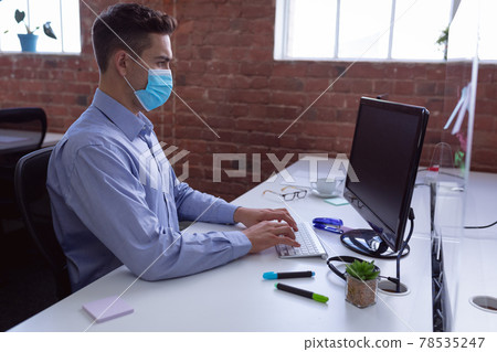 Caucasian businessman in face mask sitting at desk with hygiene screen using computer 78535247
