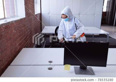 Cleaner wearing ppe suit, glasses and mask disinfecting office workspace 78535280