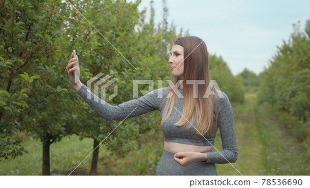 Joyful fitness woman during live stream broadcasting. A modern sports woman takes pictures on the nature smartphone, recording a video blog. Sports video vlog. Video Blog athlete. Girl blogger 78536690