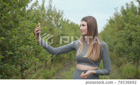 Joyful fitness woman during live stream broadcasting. A modern sports woman takes pictures on the nature smartphone, recording a video blog. Sports video vlog. Video Blog athlete. Girl blogger 78536692