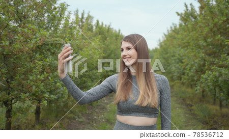 A modern sports woman takes pictures on the nature smartphone, recording a video blog. Sports video vlog. Video Blog athlete. Girl blogger points to the camera nature 78536712