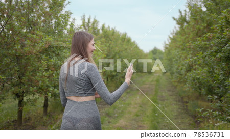 Young Attractive Sports Girl Shooting on a Phone Tree Photographed Against Nature Background. Girl blogger points to the camera nature, the concept of stories about the environment protection of trees 78536731
