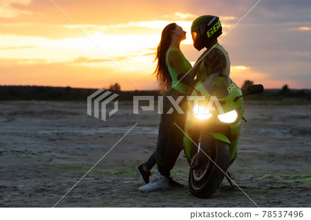 Couple embracing near motorbike on beach at sunset Couple embracing near motorbike on beach at sunset 78537496