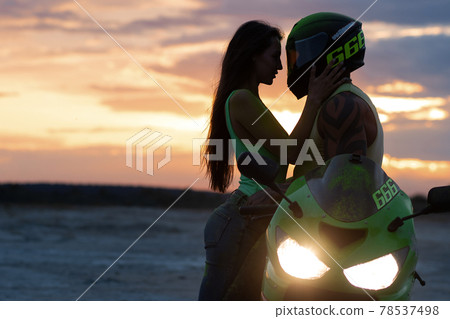 Couple embracing near motorbike on beach at sunset Couple embracing near motorbike on beach at sunset 78537498