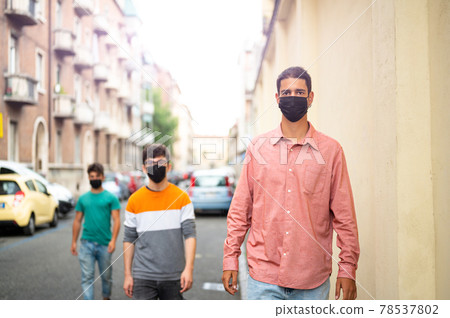 Group of friends walking on the city street with black protective mask. Pandemic time. New concept of normal lifestyle with young people covered with a protective mask. Focus on the guy on the right. Group of friends walking on the city street with black protective mask. Pandemic time. New concept of normal lifestyle with young people covered with a protective mask. Focus on the guy on the right. 78537802