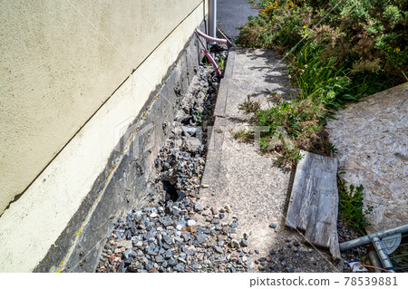 Broken pipes and footpath due to subsidence of building on a peatbog 78539881