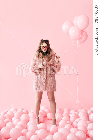 Full length portrait of glamour young woman typing on mobile smartphone over pink balloons background 78540637