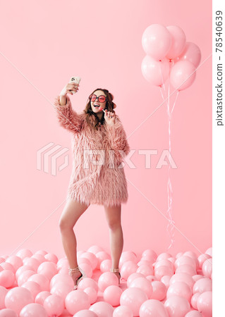 Full length portrait of glamour young woman making selfie photo on smartphone over pink balloons background Full length portrait of glamour young woman making selfie photo on smartphone over pink balloons background 78540639