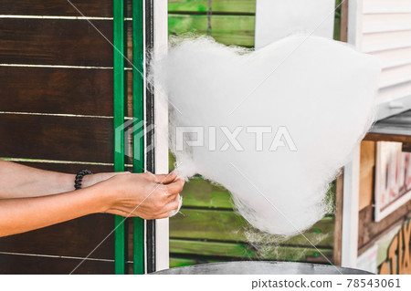 The girl's hands are held on a stick and make cotton candy on the street background 78543061