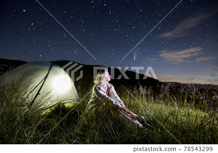 Beautiful young woman sitting on grass under night starry sky. Beautiful young woman sitting on grass under night starry sky. 78543299