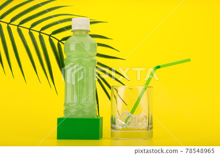 Green tropical summer cocktail on green pedestal with glass filled with ice cubes and green straw on yellow background  78548965