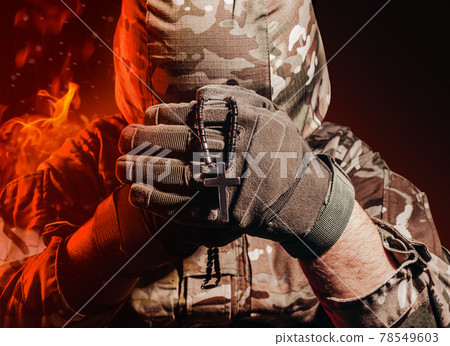 Soldier in uniform and helmet holding a cross necklace. 78549603