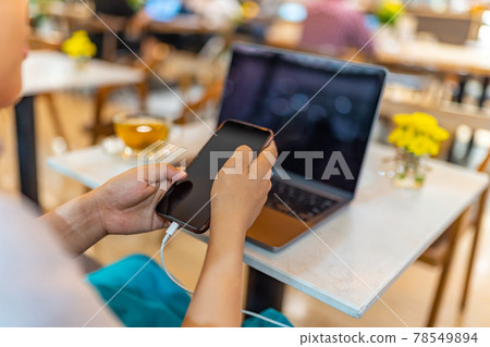 Young woman using cellphone while charging battery  78549894
