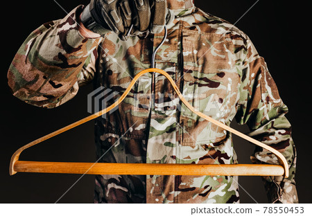 Soldier in gloves holding wooden shirt hanger. 78550453