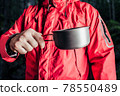 Hiker in red jacket holding metal cup. 78550489