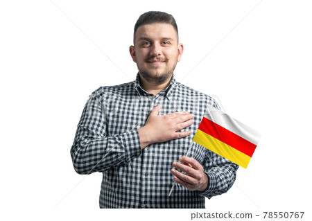 White guy holding a flag of South Ossetia and holds his hand on his heart isolated on a white background With love to South Ossetia White guy holding a flag of South Ossetia and holds his hand on his heart isolated on a white background With love to South Ossetia 78550767