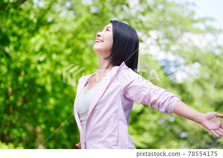 穿著運動服在新鮮綠色植物中伸展身體的中年婦女 78554175