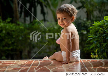 a charming toddler sits on the steps of a house in the sunlight. back view a charming toddler sits on the steps of a house in the sunlight. back view 78555262