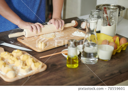 Female hands roll out a piece of dough with a rolling pin for making ravioli or dumplings on a wooden table sprinkled with flour. A step-by-step recipe for cooking ravioli or dumplings Female hands roll out a piece of dough with a rolling pin for making ravioli or dumplings on a wooden table sprinkled with flour. A step-by-step recipe for cooking ravioli or dumplings 78559601