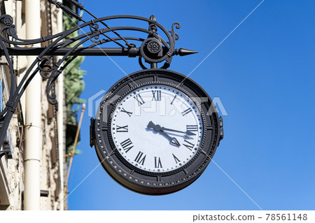 Antique round clock with Roman numerals hang on the street of the city Antique round clock with Roman numerals hang on the street of the city 78561148