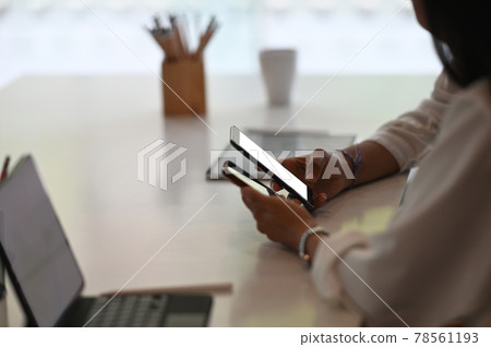 Cropped shot of young female freelancer using smartphone in modern office. Cropped shot of young female freelancer using smartphone in modern office. 78561193