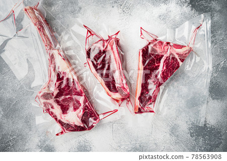 Raw uncooked beef steaks in vacuum packed air sealed sous vide bag, tomahawk, t bone and club steak cuts, on gray stone background, top view flat lay Raw uncooked beef steaks in vacuum packed air sealed sous vide bag, tomahawk, t bone and club steak cuts, on gray stone background, top view flat lay 78563908